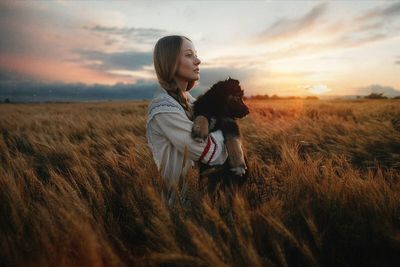 Woman with dog on field against sky during sunset