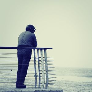 Rear view of man standing by sea against clear sky