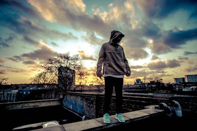 Man standing on retaining wall against cloudy sky during sunset
