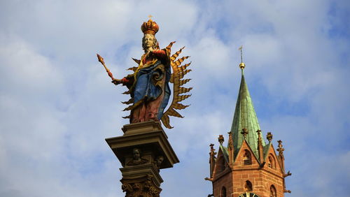 Low angle view of statue and church against cloudy sky