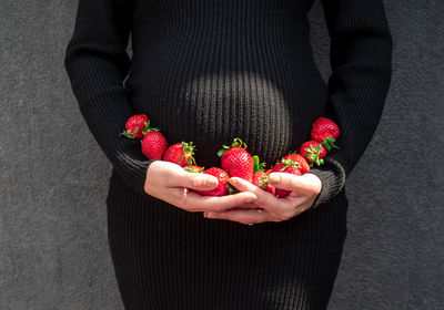 Midsection of a pregnant woman holding strawberries around her belly