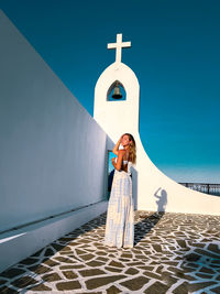 Woman in long dress standing in front of white washed greek chapel on the island of rhodes, greece 