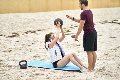 Fitness instructor assisting woman in exercising at beach