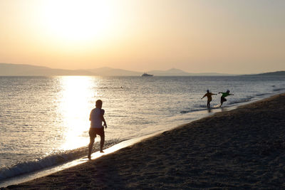 People on beach against sky during sunset