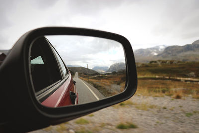 Road and landscape reflecting on side-view mirror of car against sky