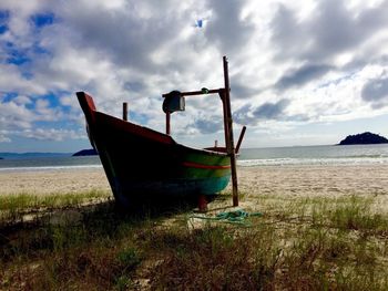 Boat moored on beach against cloudy sky