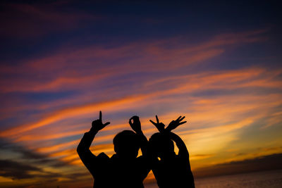 Silhouette people against orange sky during sunset