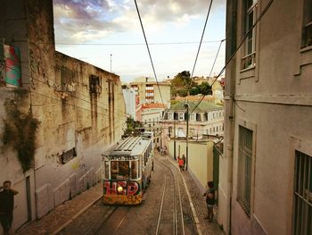 Tram cars on street by railroad tracks in city against sky