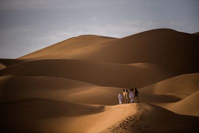 Men with camels on sand dune in desert against sky