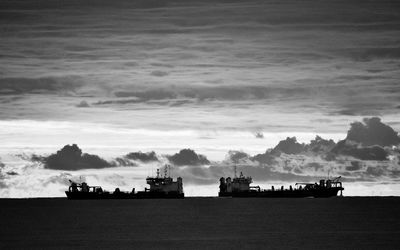 Silhouette boats on sea against sky at dusk