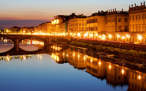 Illuminated bridge over river by buildings against sky at night