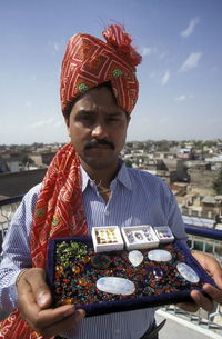 Portrait of vendor holding semi-precious gems against sky