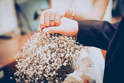 Midsection of couple holding hands over flower bouquet