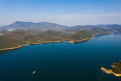 Aerial view of sea and mountains against blue sky
