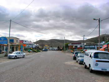 Cars on city street against cloudy sky