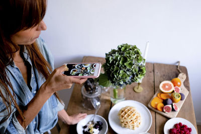 High angle view of female blogger photographing food at table through mobile phone by wall