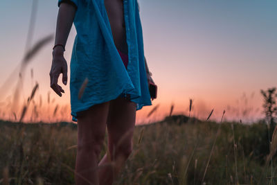 Midsection of woman standing on field against sky during sunset