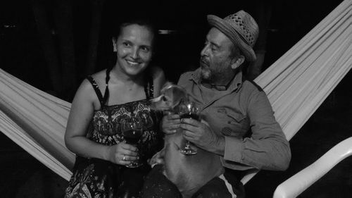 Happy couple sitting on hammock while holding wineglasses at night