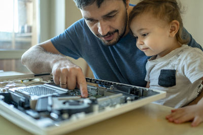 Cute boy looking at father repairing computer on table