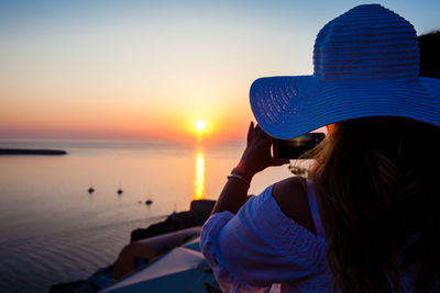 Rear view of woman looking at sea against sky during sunset