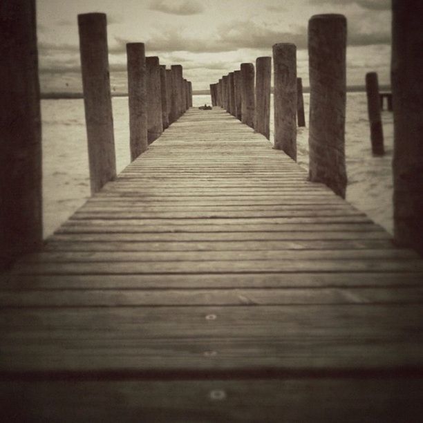 wood - material, in a row, wooden, the way forward, diminishing perspective, pier, sky, built structure, wood, architecture, wooden post, boardwalk, surface level, sea, no people, outdoors, day, vanishing point, tranquility, cloud - sky