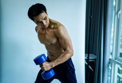 Shirtless muscular man lifting dumbbells