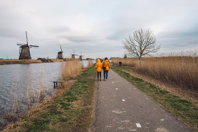 Rear view of men walking on road against sky and windmills