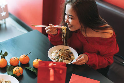 Beautiful asian woman in red clothes eating noodles with chopsticks in chinese vietnamese restaurant
