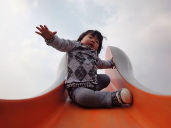 Low angle view of cute baby girl sitting on orange slide against sky