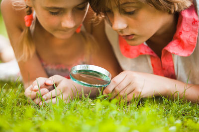 Boy and girl with magnifying glass on grass outdoors