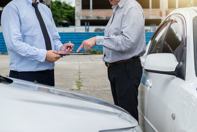 Midsection of dealer and customer standing by cars