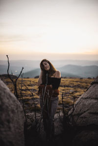 Woman posing on rock against sky during sunset