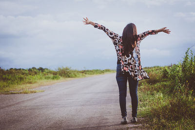 Woman standing by road on field against sky