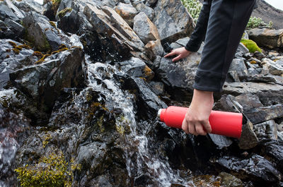 Cropped hand pouring red bottle from stream on rock