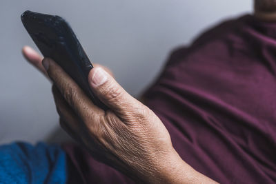 Senior ethnic male in glasses relaxing on couch in living room and reading messages on smartphone