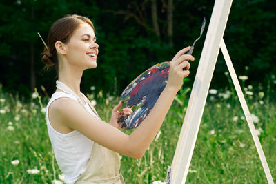 Side view of young woman holding sunglasses against plants