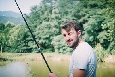 Portrait of young man holding fishing rod by plants