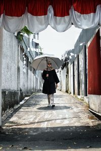 Mature woman with umbrella walking in alley