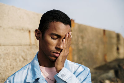 Man with head in hands and eyes closed standing outdoors