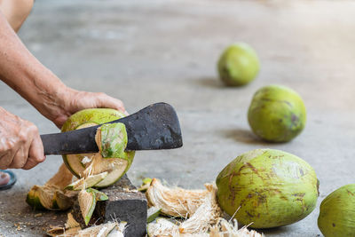 Low section of man cutting coconut with knife on floor