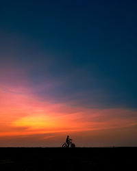Silhouette people riding bicycle on road against sky during sunset