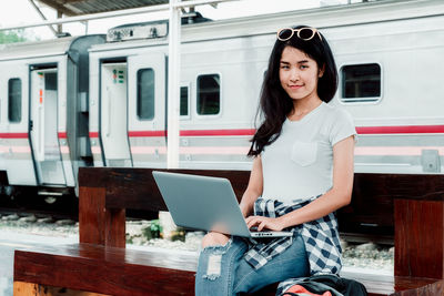 Full length of young woman using phone while standing on train