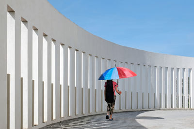 Rear view of a boy walking with a multi colored umbrella against white pillars