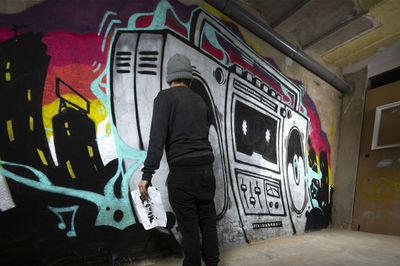 Rear view of man standing against graffiti wall