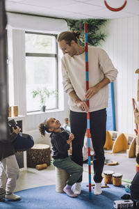 Smiling male teacher looking at female student sitting on drum at child care center