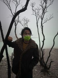 Portrait of man wearing surgical mask while standing against trees during winter