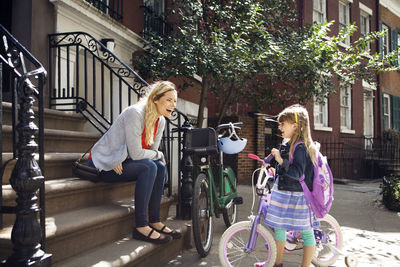 Cheerful mother and daughter with bicycles talking on steps