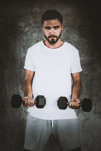 Portrait of man holding dumbbells against wall