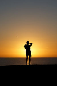 Rear view of silhouette man standing at beach against sky during sunset