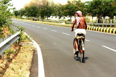 Full length rear view of man riding bicycle on road